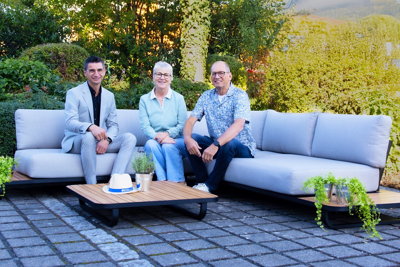Das Bild zeigt die Gewinnerin der Landpartie Verlosung, ihren Mann und einen Vertreter der VR-Bank Main-Kinzig Büdingen. Die drei Personen sitzen auf der verlosten Gartenlounge im Garten der Gewinnerin. 