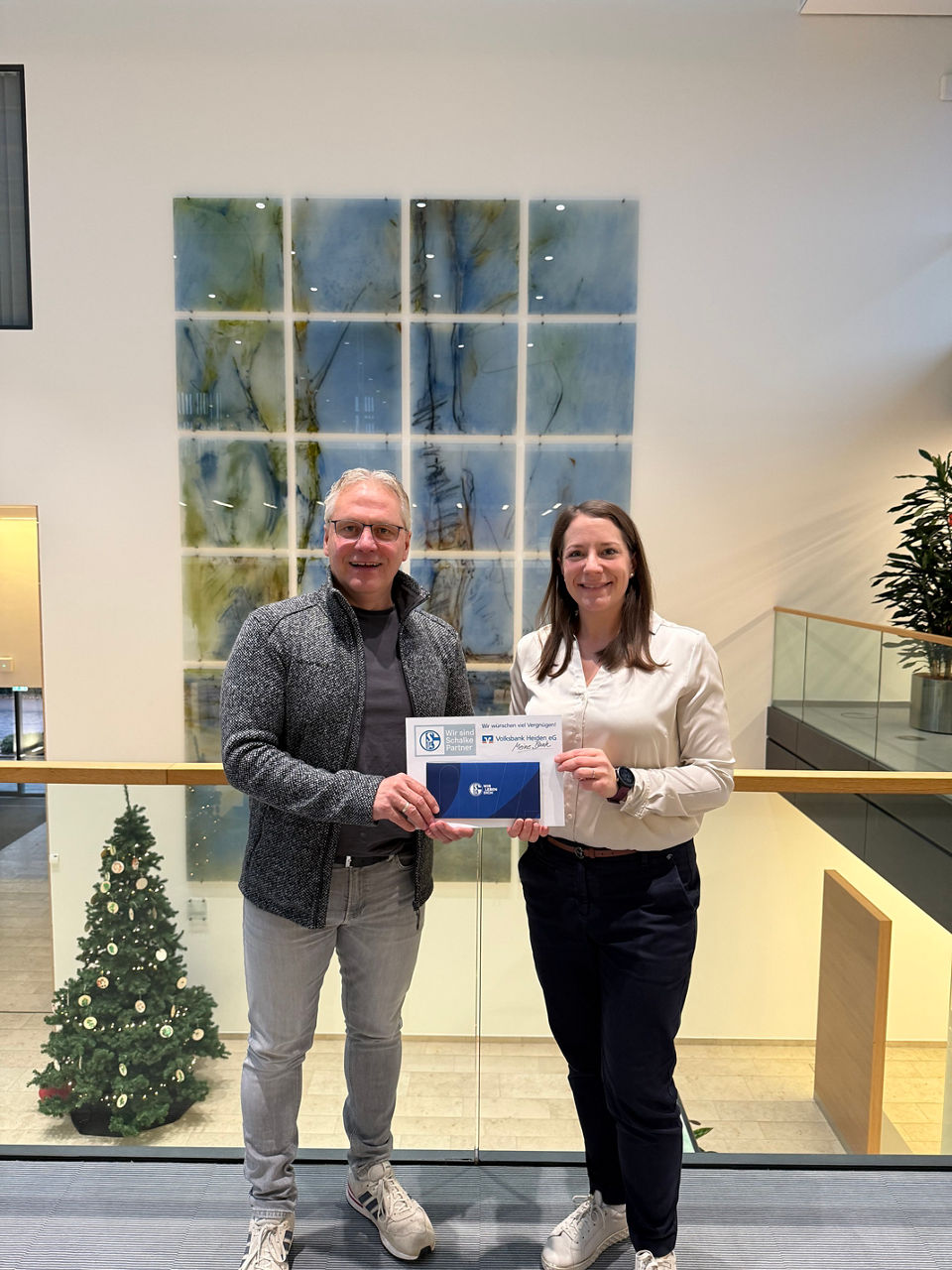 Eine Frau und ein Herr lächeln in die Kamera, zeigen den Daumen hoch und halten gemeinsam ein Dokument in den Händen.