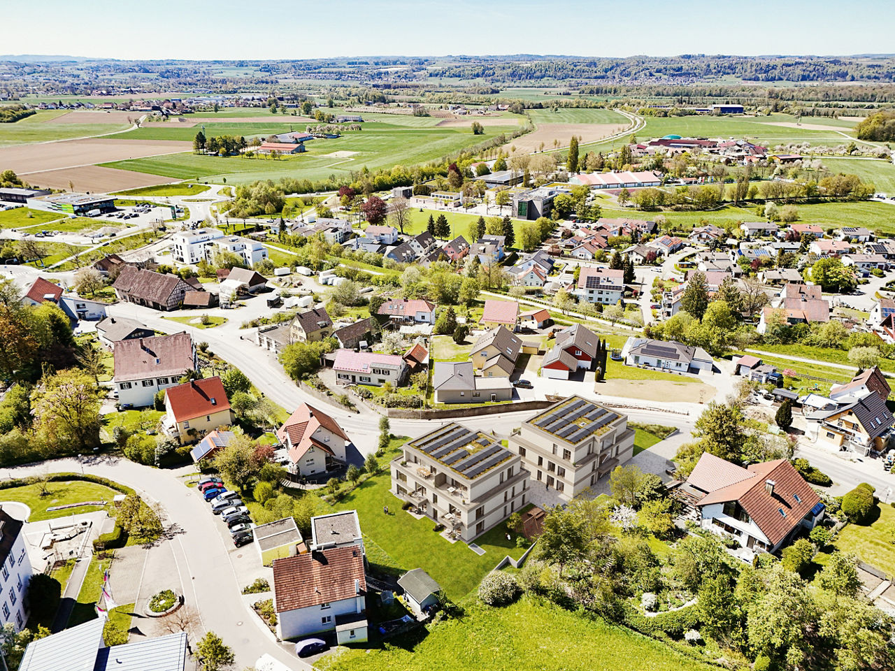 Luftaufnahme eines Wohngebiets mit eingefügter Visualisierung von zwei modernen Mehrfamilienhäusern in ländlich geprägter Umg