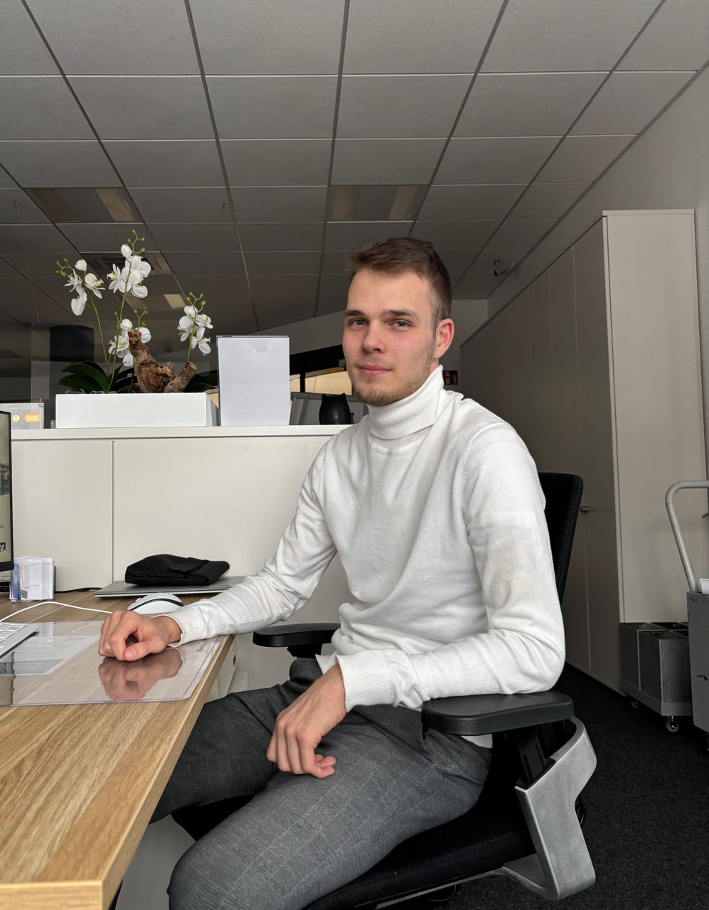 Mitarbeitener sitzt   auf einem Bürostuhl mit einem Arm auf  seinem Schreibtsich