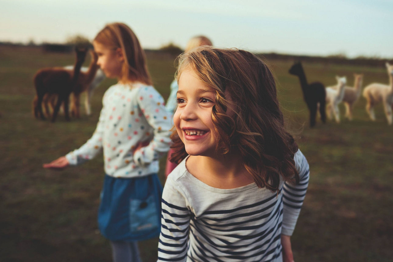Fröhliche Kinder stehen auf einer Wiese mit Alpakas.