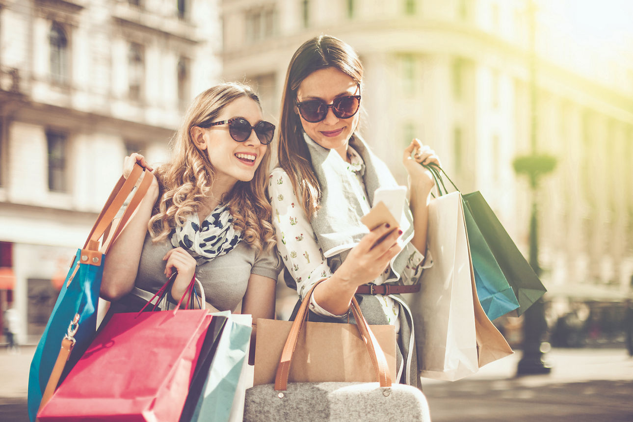 Zwei Mädchen beim shoppen mit Einkaufstüten in der Hand und schauen auf ein Handy