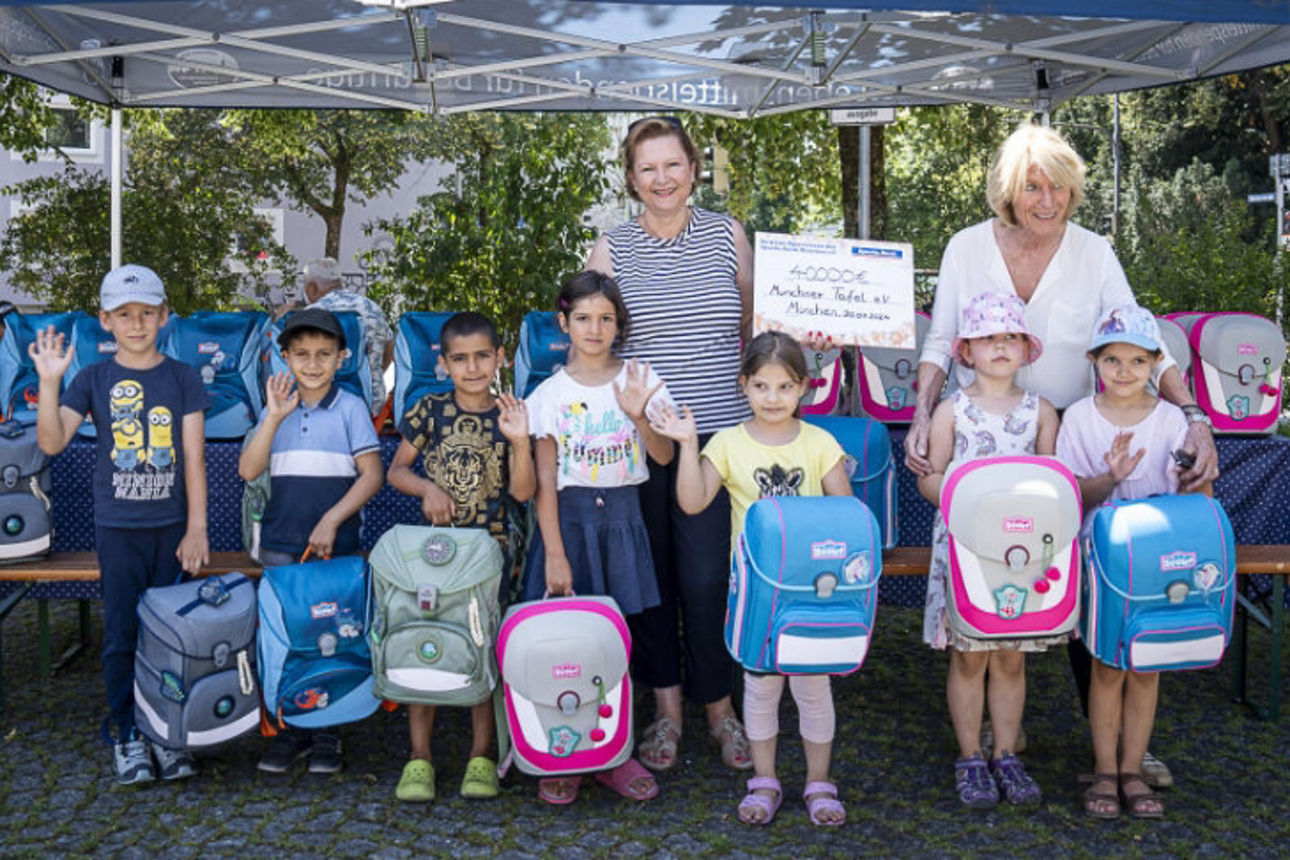 Gruppenbild von 2 Frauen mit einigen Kindern, die neue Schulranzen geschenkt bekommen