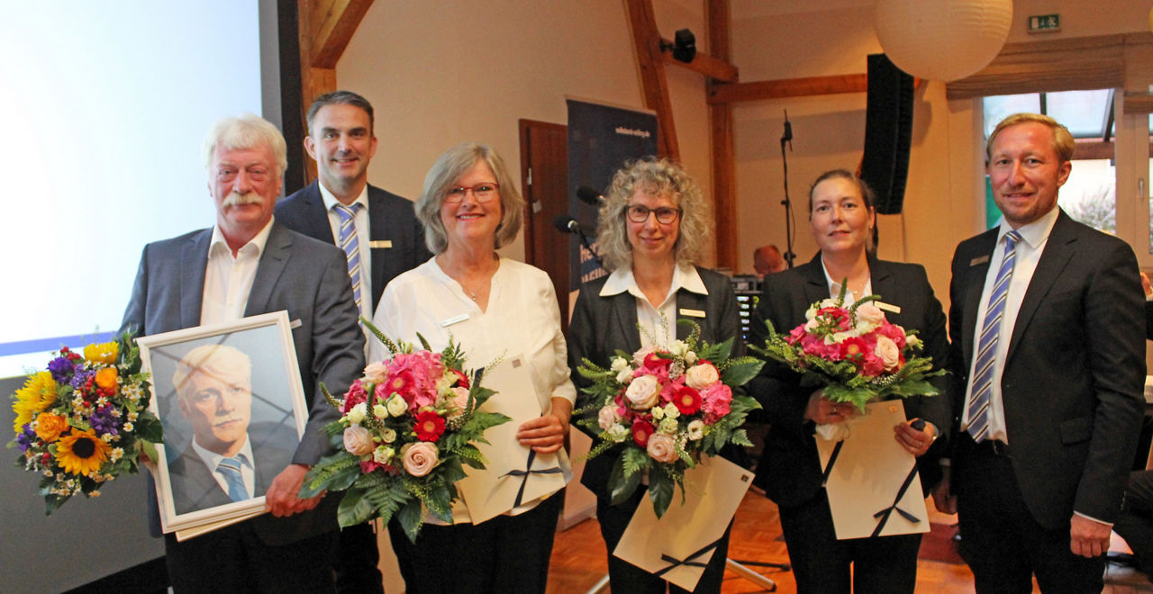Die Mitarbeiterehrung, sechs Personen mit Blumensträußen und Geschenken. 