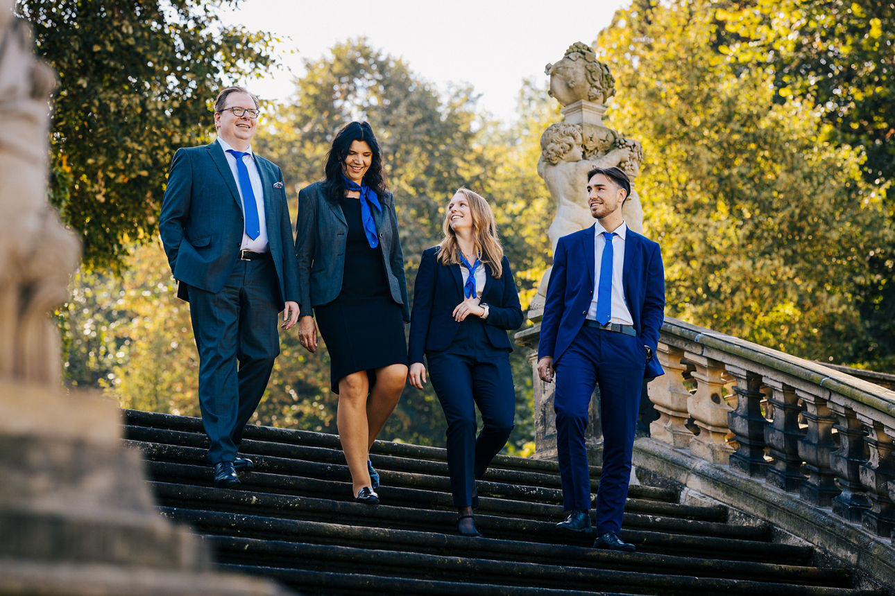 Mitarbeiter in Businesskleidung gehen miteinander sprechend und lachend eine Treppe im Barockgarten herunter