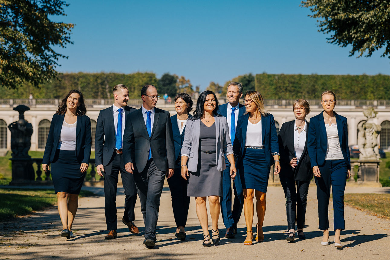 Gruppe von Menschen in Businesskleidung geht durch einen barocken Park und unterhält sich dabei locker