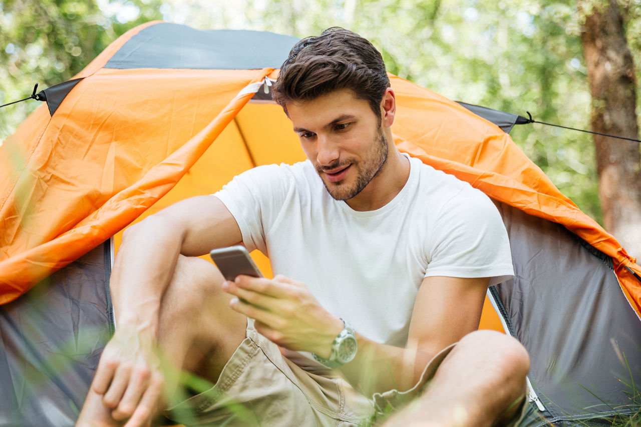 Junger Mann vor einem Zelt mit Smartphone in der Hand