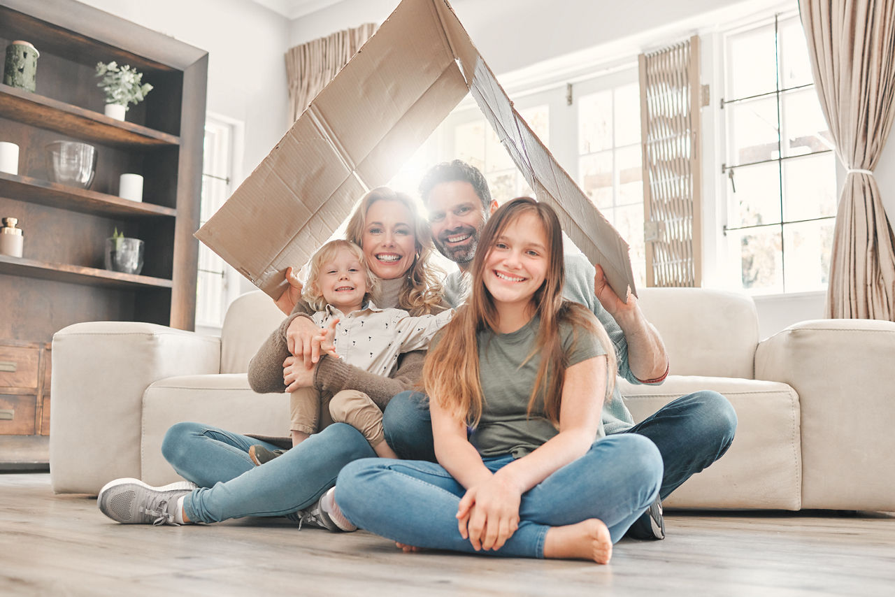 Glückliche Familie, die spielerisch Pappe über dem Kopf hält, sodass es aussieht wie ein Dach
