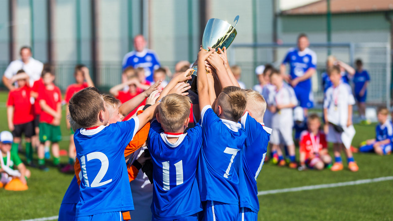Eine junge Fußballmannschaft freut sich über einen Sieg und hält einen Pokal in die Höhe.