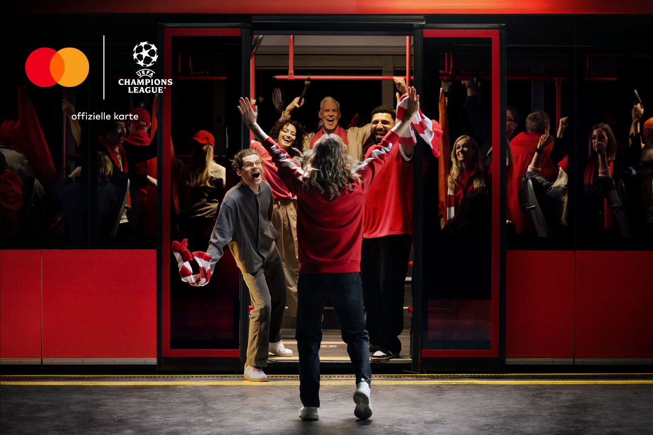 Jubelnde Fans mit roten Schals in einer U-Bahn. Logos von UEFA und Mastercard oben links