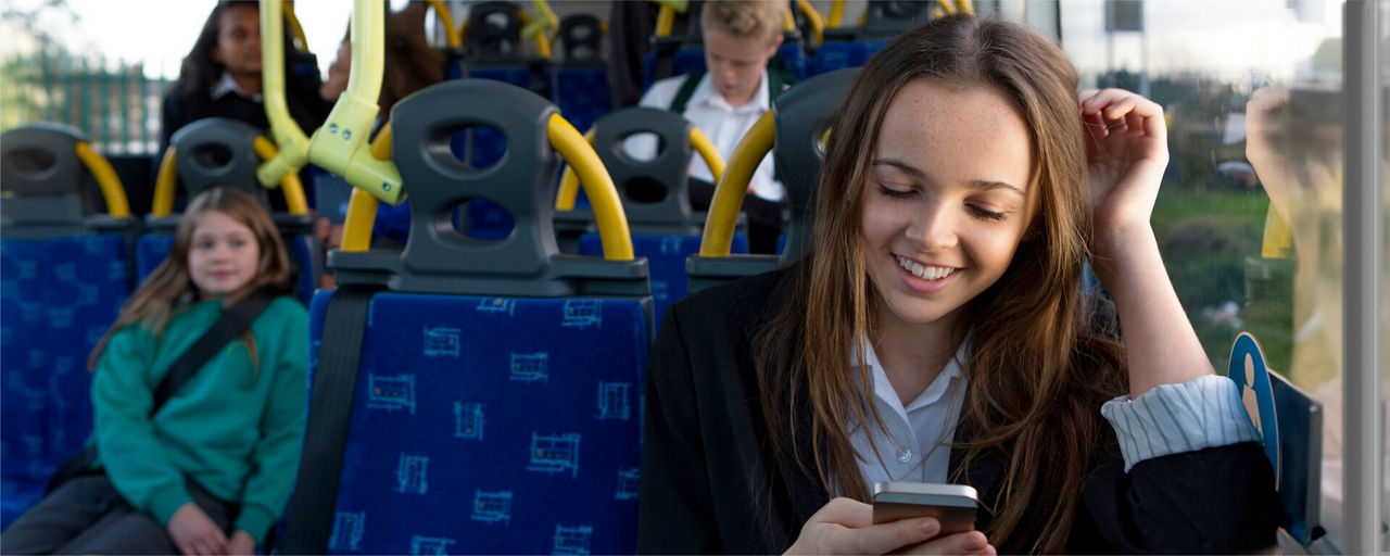 Lachendes jugendliches Mädchen mit Smartphone in der Hand in der Straßenbahn