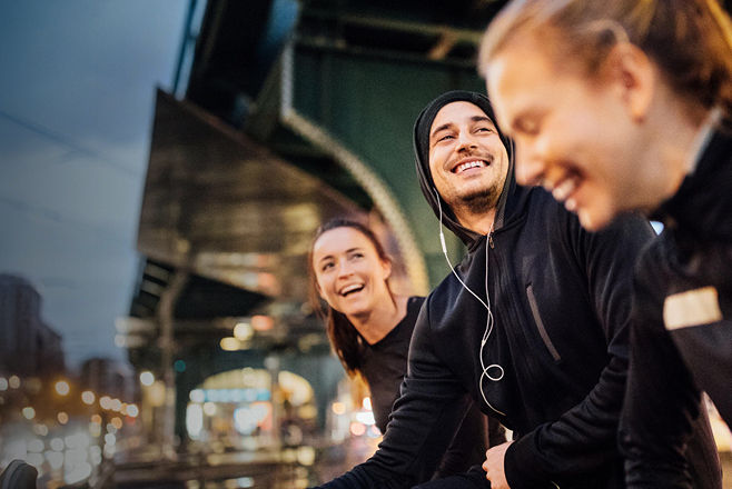 Drei Personen mit dunklen Oberteilen lachen vor beleuchtetem Hintergrund