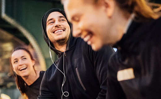 Drei Personen mit dunklen Oberteilen lachen vor beleuchtetem Hintergrund