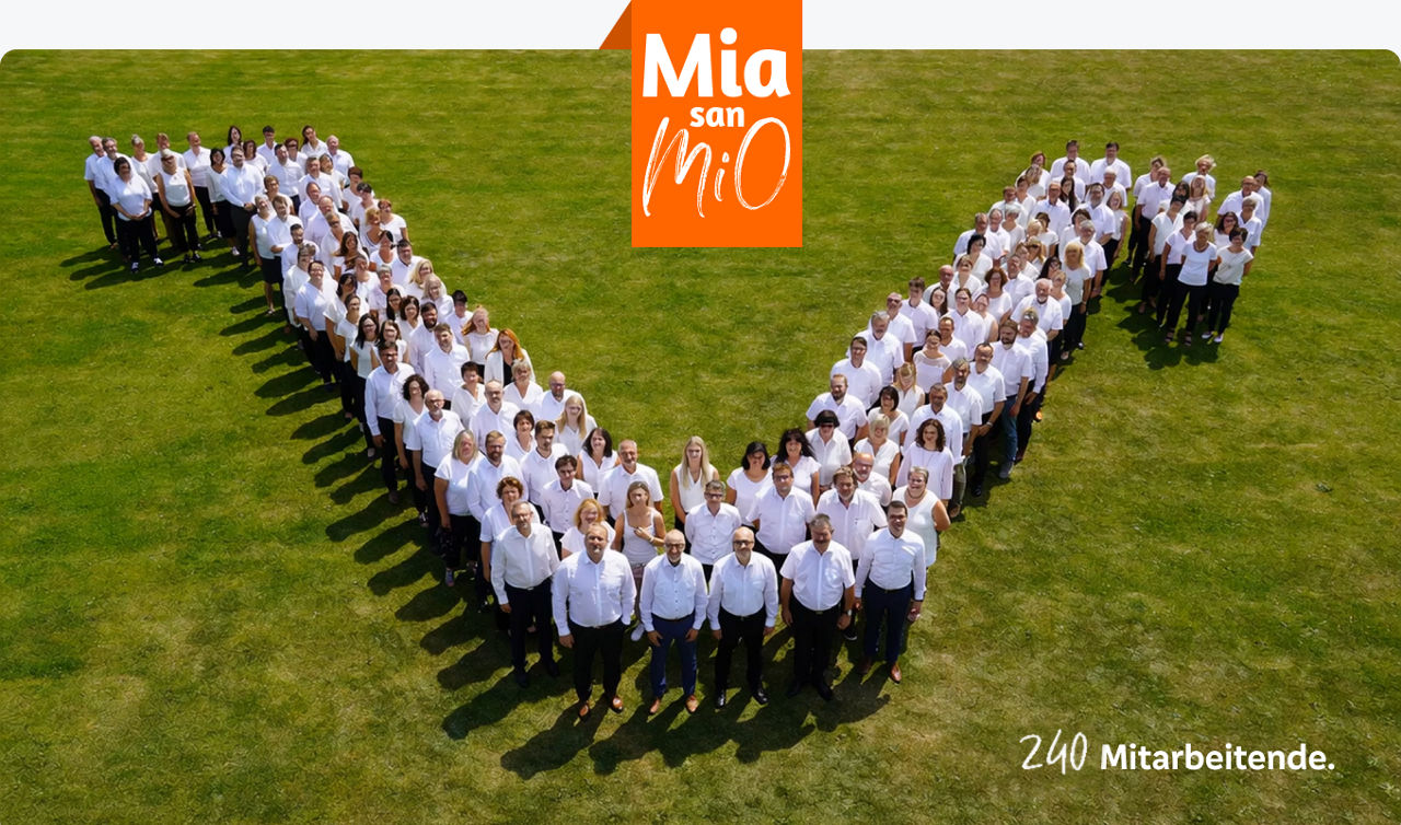 MiO Mitarbeiter stehen als VR-V auf Rasen, Text: 200 Mitarbeitende