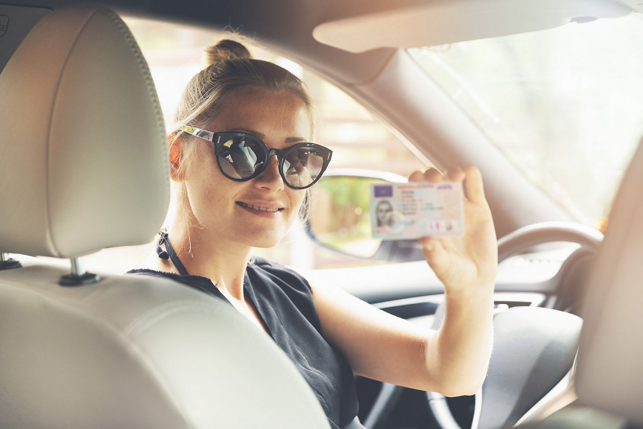Mädchen sitzt im Auto und hat ihren Führerschein in ihrer Hand