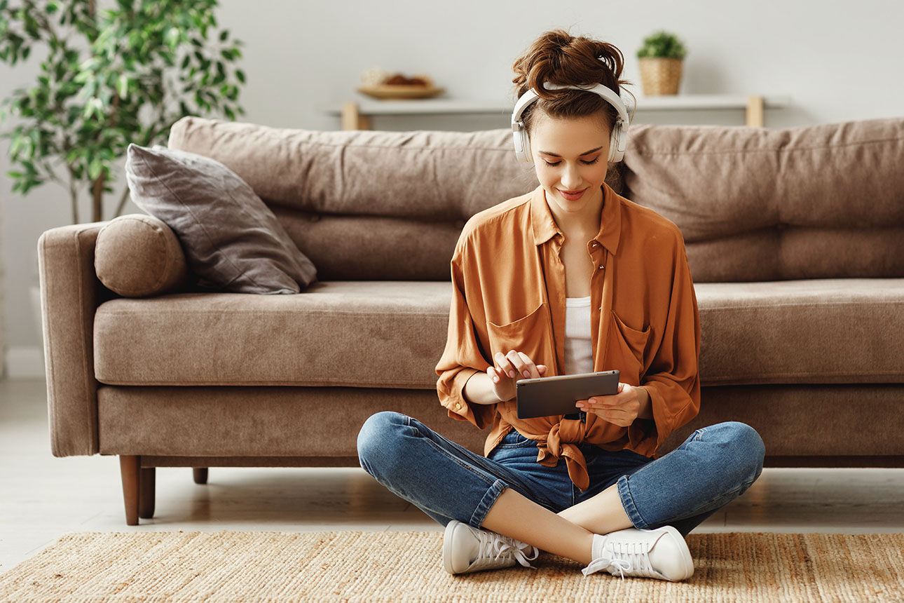 Frau im Schneidersitz vor Sofa mit iPad auf dem Schoß