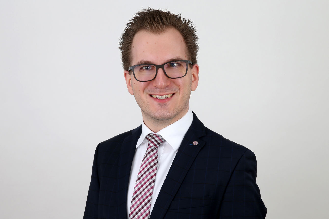 Ein lächelnder Mann in einem Anzug schaut in die Kamera.
