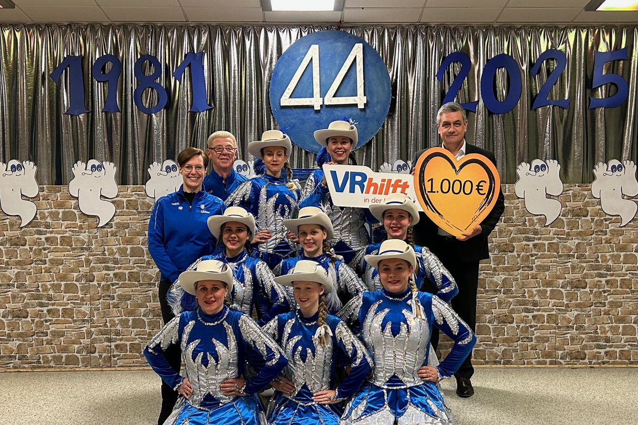 Das Bild zeigt acht junge Frauen in blauen und silbernen Tanzkostümen, die vor einer silbernen Kulisse mit den Zahlen 1981 un