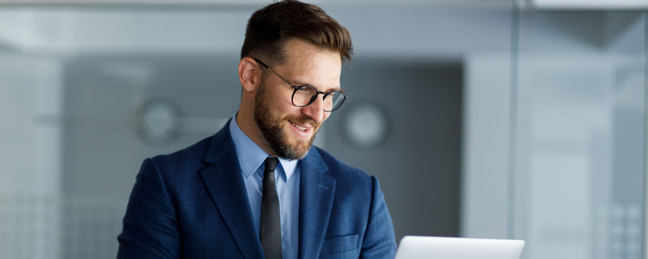 Eine Mann mittleren Alters in einem blauen Anzug steht in einem modernen Büro und hält einen Laptop.