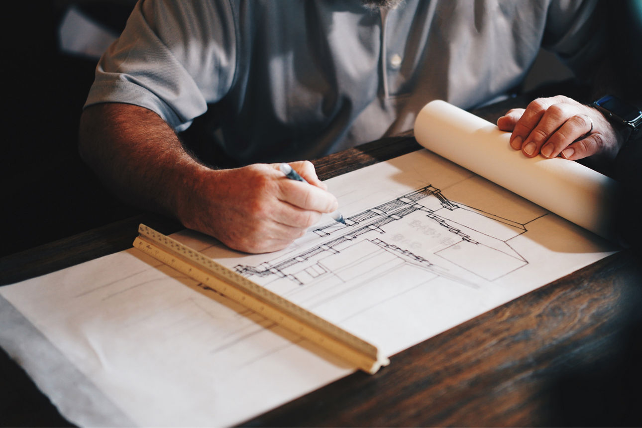 Mann sitzt am Tisch und zeichnet auf einem Blatt Papier