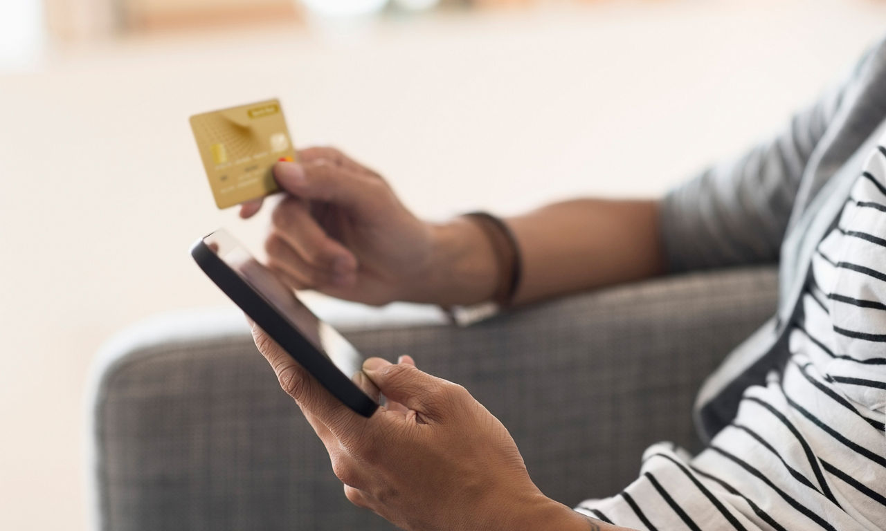 Mann sitzt auf dem Sofa und hält ein Smartphone und eine Karte in der Hand