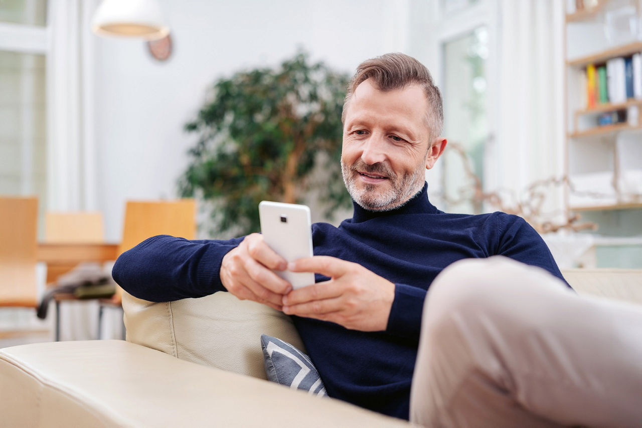 Mann sitzt auf dem Sofa und ist mit seinem Smartphone beschäftigt