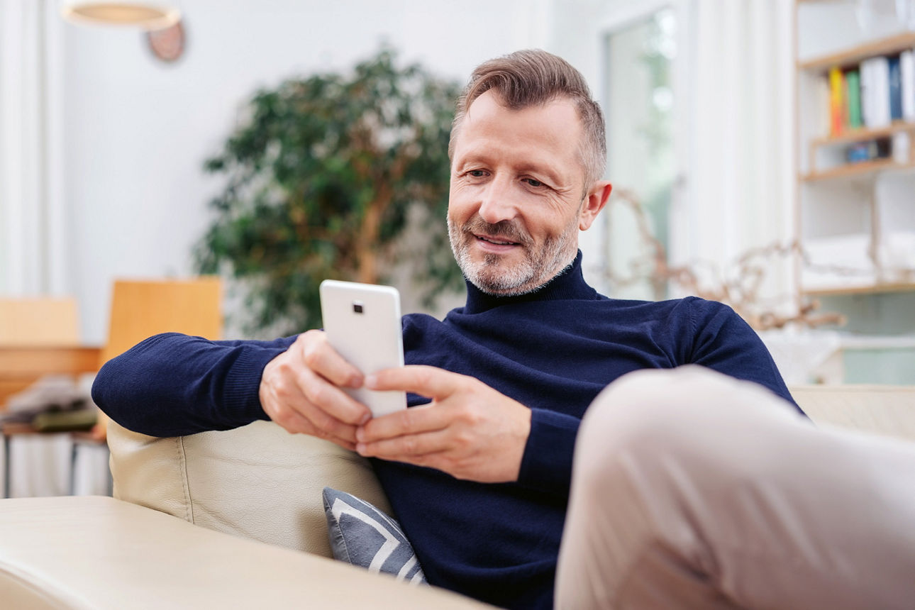 Mann sitzt auf dem Sofa und ist mit seinem Smartphone beschäftigt