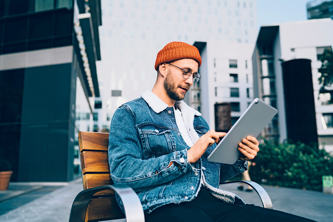 Man mit roter Hipster Mütze am Tisch und schaut aufs Tablet