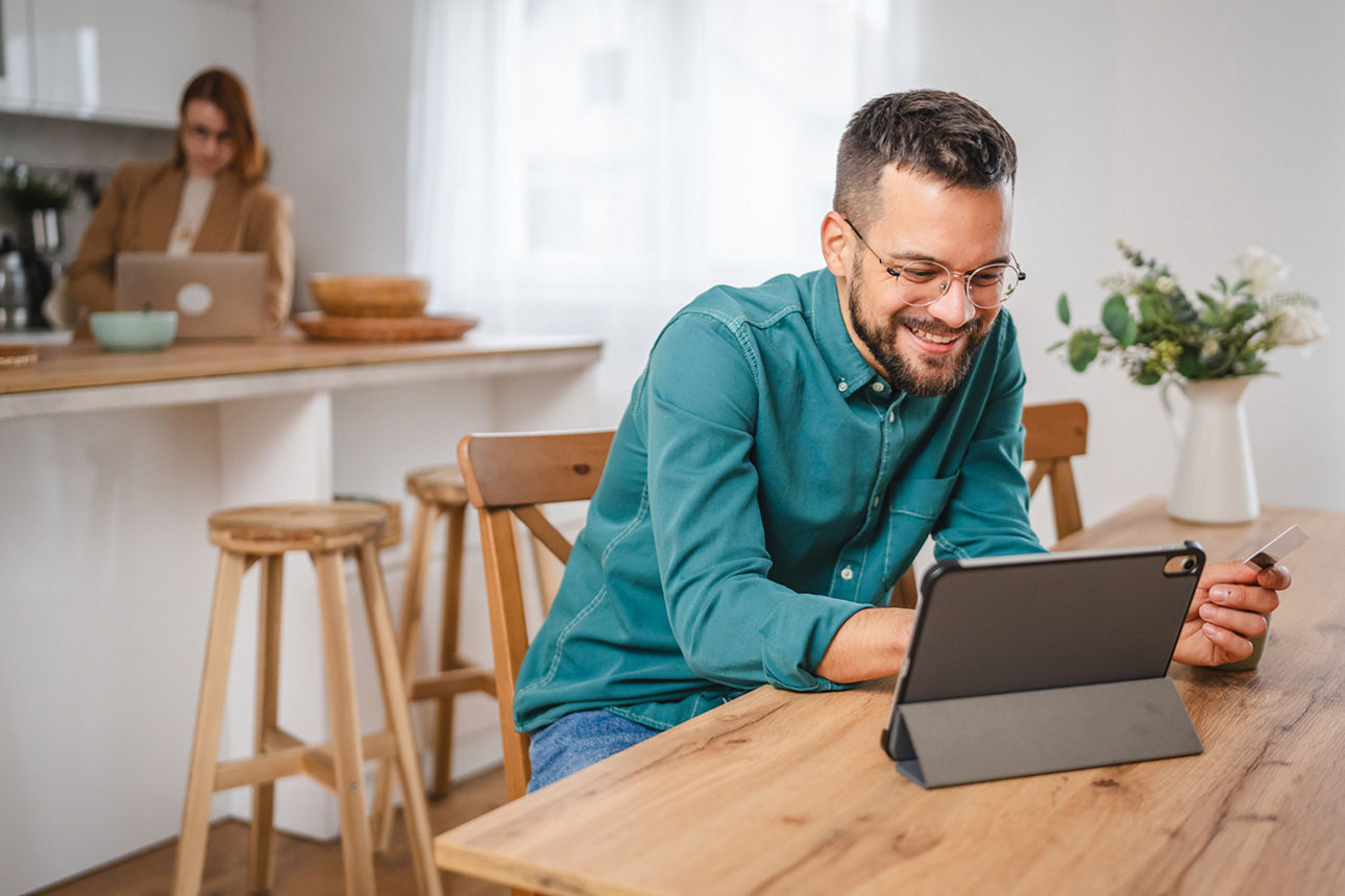 Mann sitzt vor einem Tablet und unterhält sich lächelnd