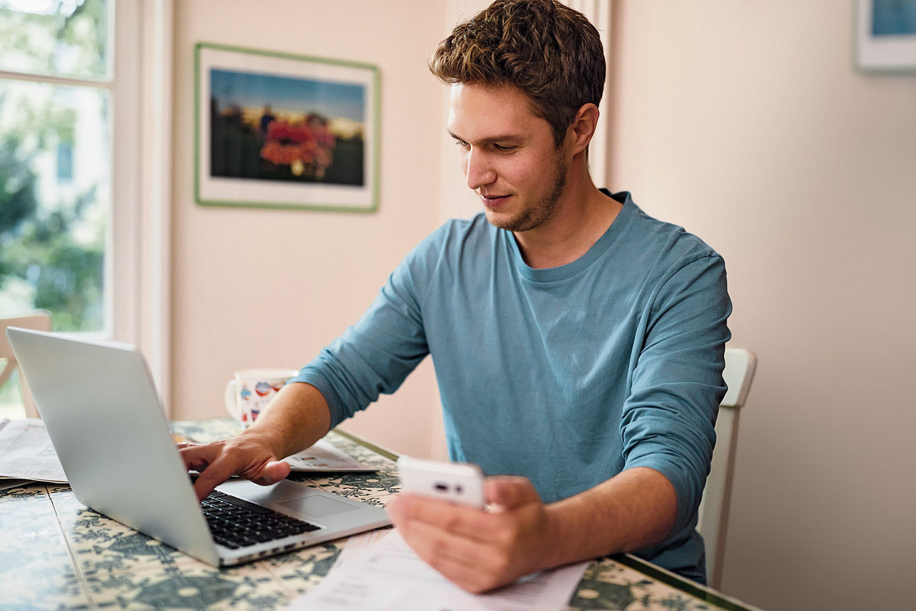 Mann an einem Schreibtisch schaut in einen Laptop und lehnt sich entspannt zurück