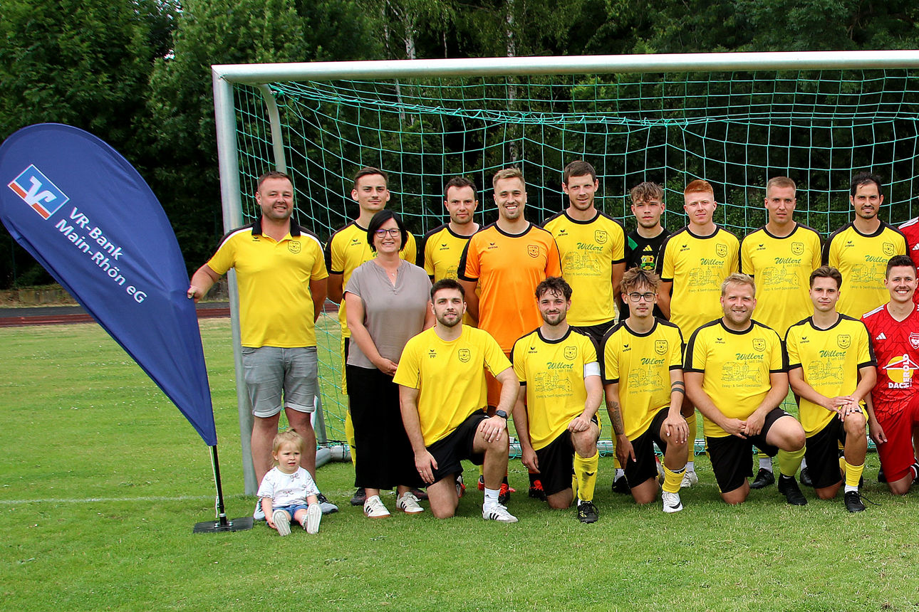 Zwei Fußballmannschaften stehen und knien vor einem Tor für eine Spendenübergabe