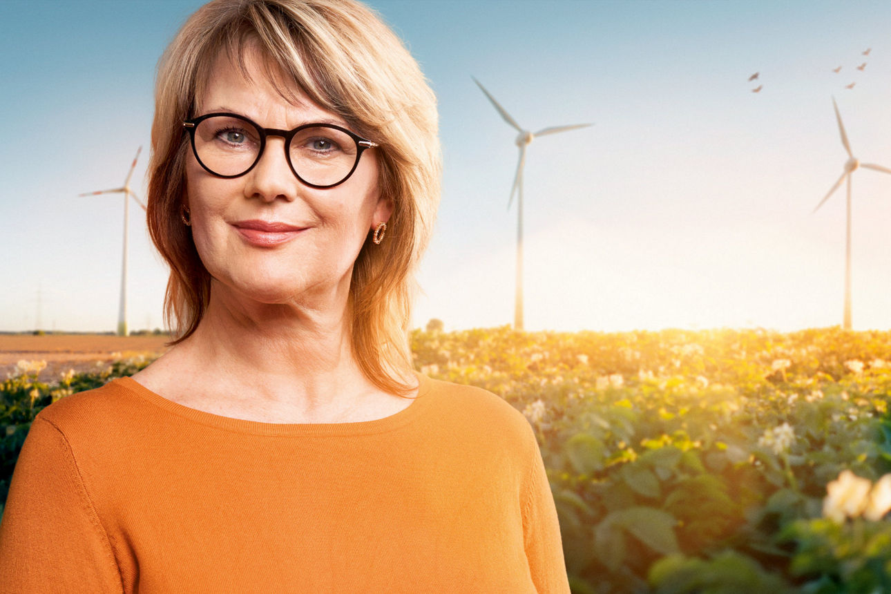 Frau steht vor einem Feld, im Hintergrund sind Windräder zu sehen