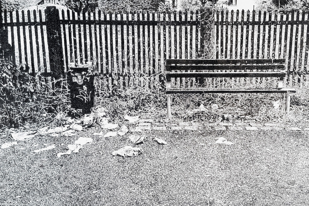 Kunstwerk (Gartenzaun, davor eine Holzbank mit Abfalleimer)