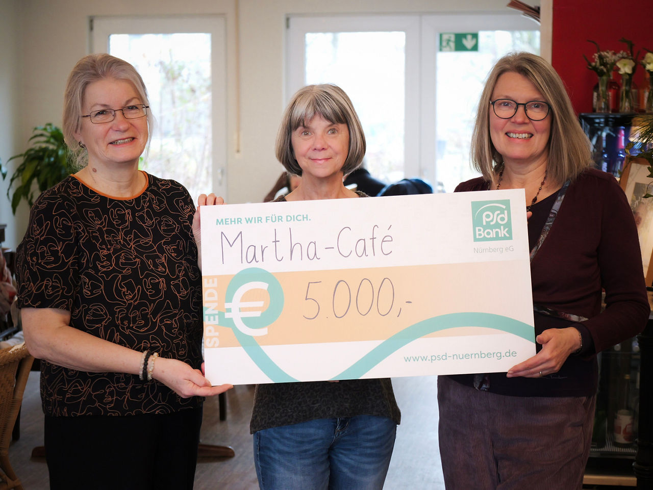 Drei Mitarbeiter:innen des Martha Cafés nehmen einen Spendenscheck über 5.000 Euro entgegen