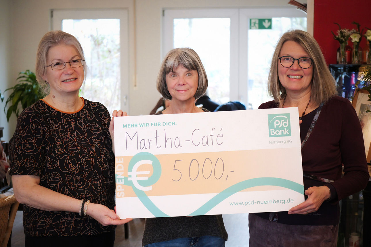Drei Mitarbeiter:innen des Martha Cafés nehmen einen Spendenscheck über 5.000 Euro entgegen