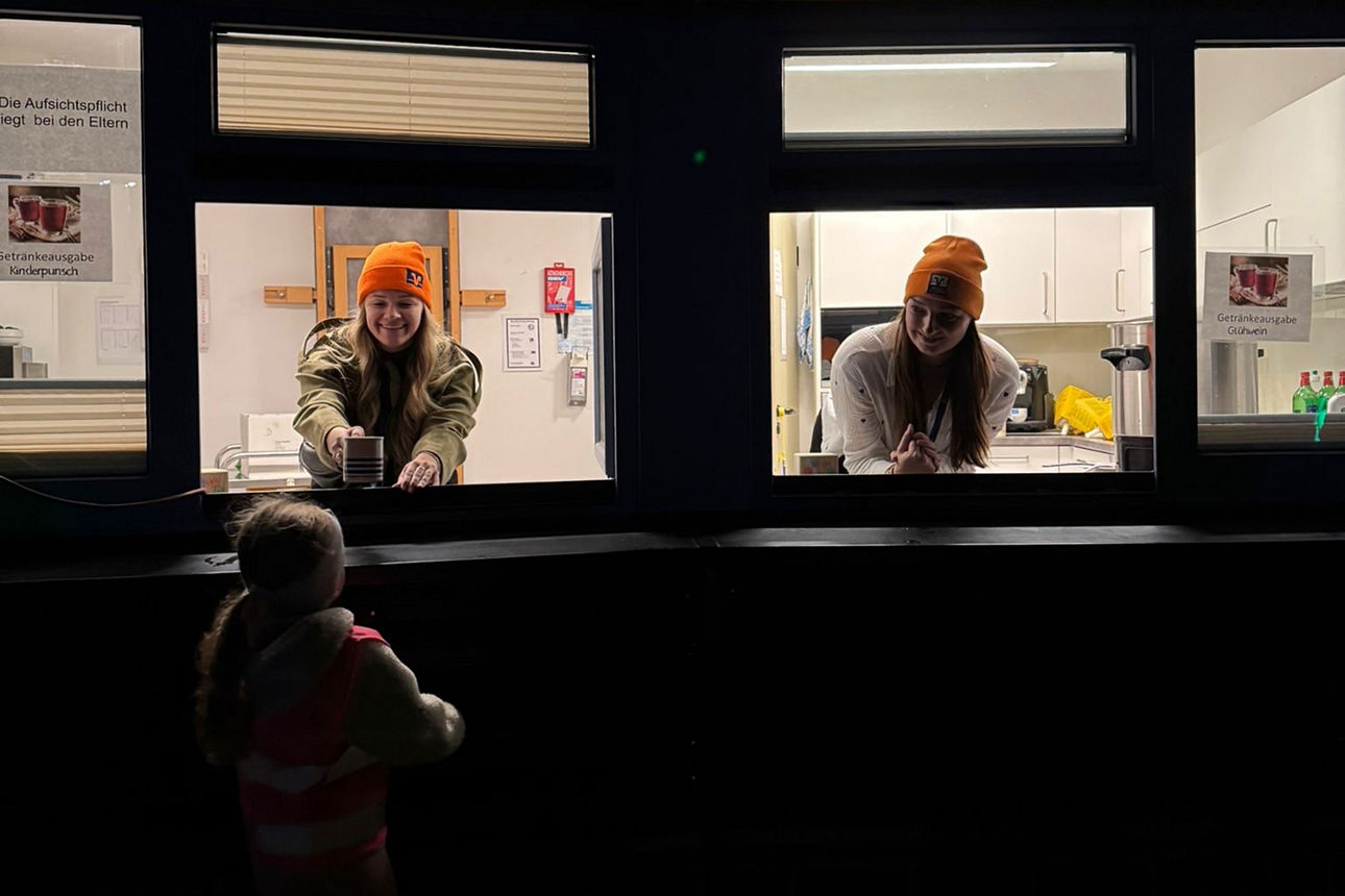 Nicole Schult und Lara Berger schauen aus zwei Fenstern, um von dort Kakau, Fruchtpunsch und Glühwein an die Teilnehmer des St. Martinumzuges zu verteilen.