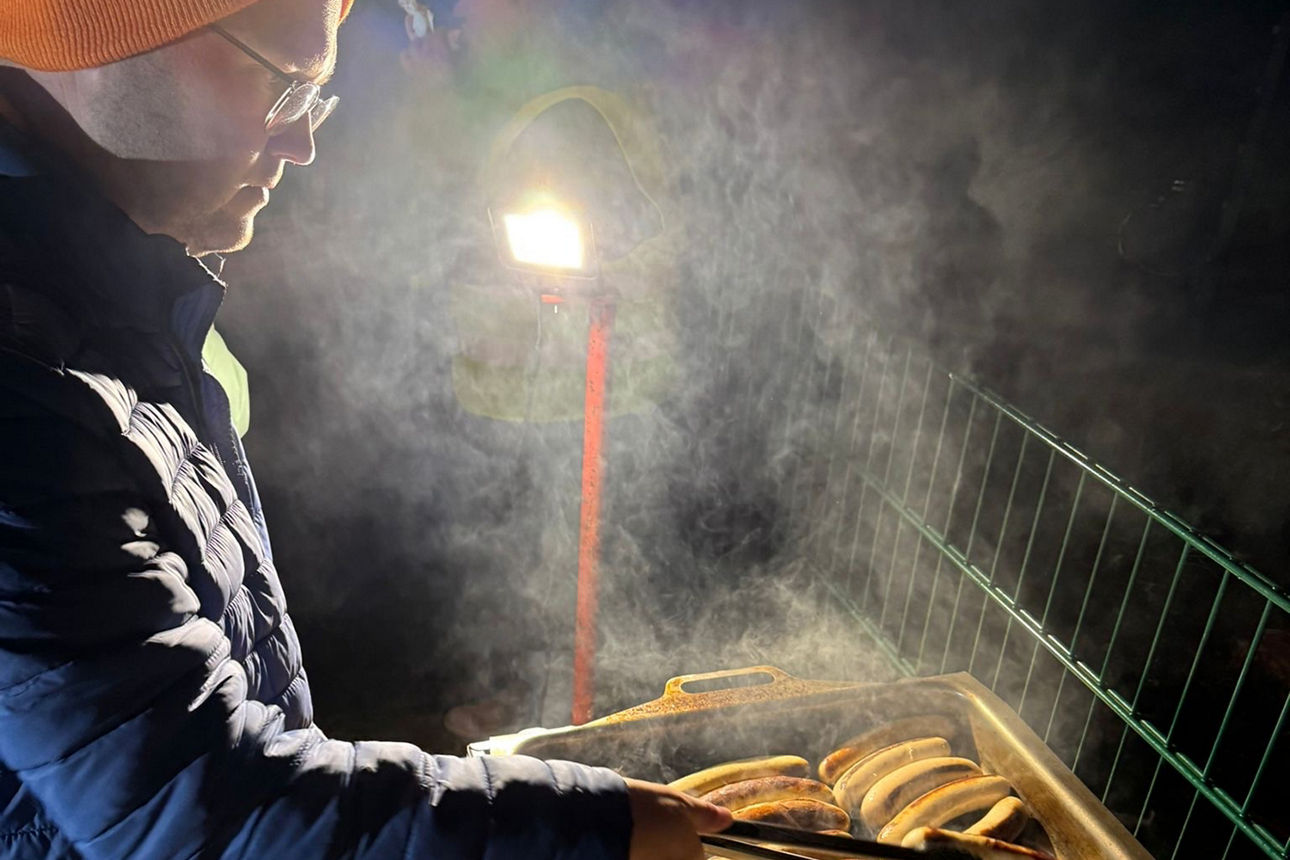 Sebastian Rau steht am Grill und grillt Würstchen.
