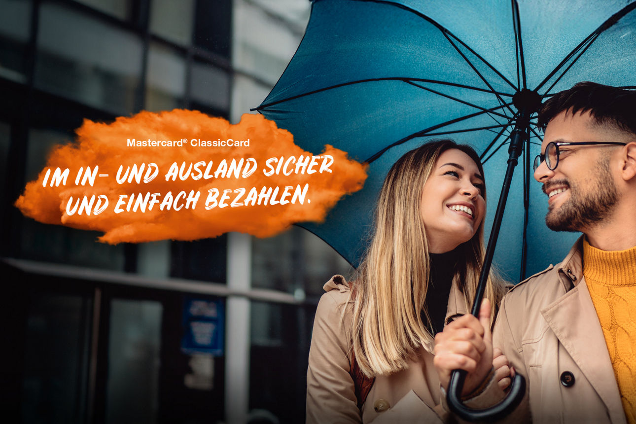 Pärchen unter einem Regenschirm die sich anlächeln. Links im Bild steht auf einer orangenen Fläche "Mastercard® ClassicCard: Im In- und Ausland sicher und einfach bezahlen."