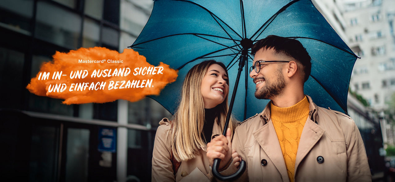Pärchen unter einem Regenschirm die sich anlächeln. Links im Bild steht auf einer orangenen Fläche "Mastercard® Classic: Im In- und Ausland sicher und einfach bezahlen."