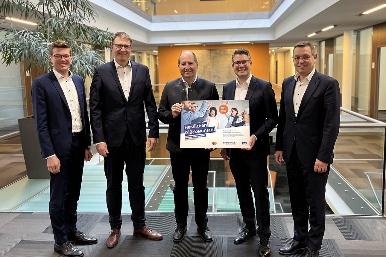 FÜnf Männer in modernem Hauptstellengebäude der Freisinger Bank präsentieren stolz ein Glückwunsch-Plakat