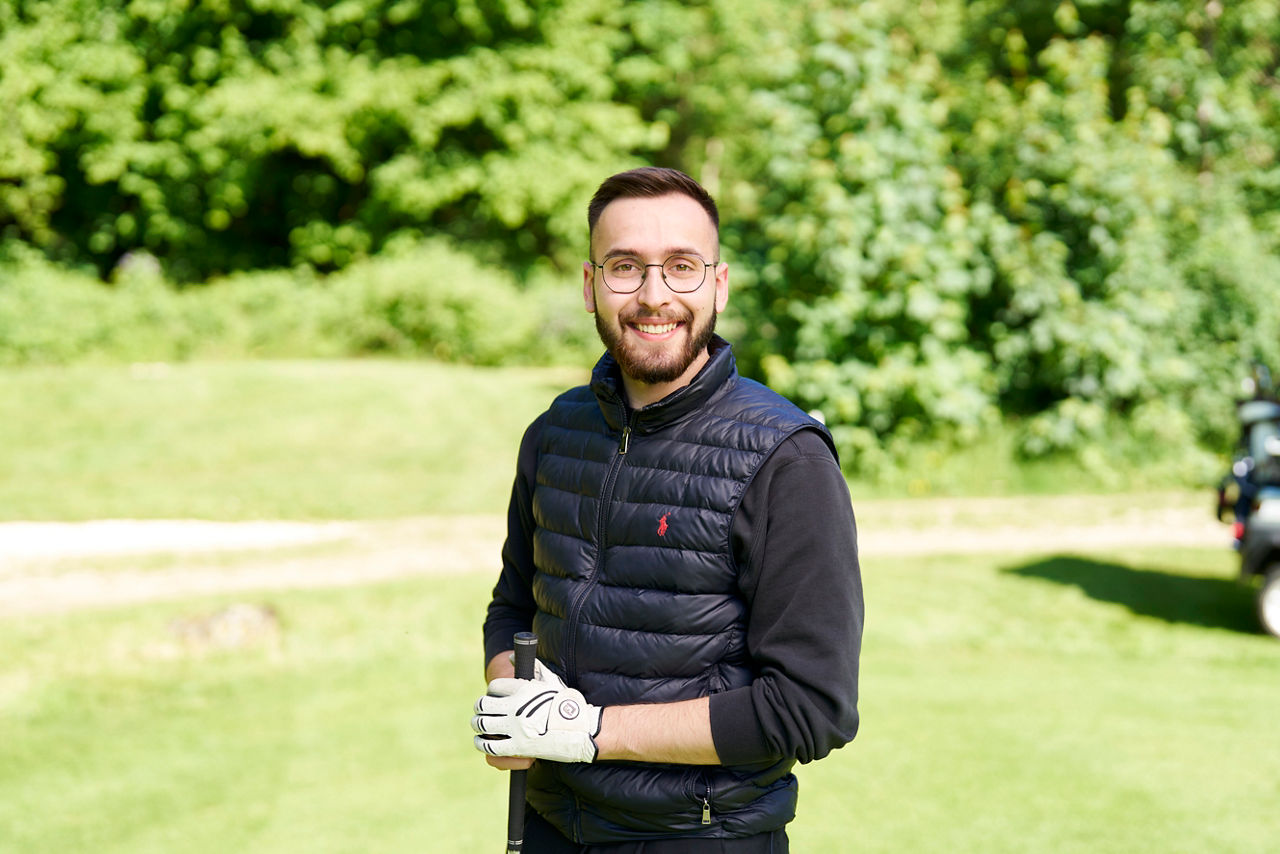 Max Müller steht auf einem Golfplatz und lacht in die Kamera