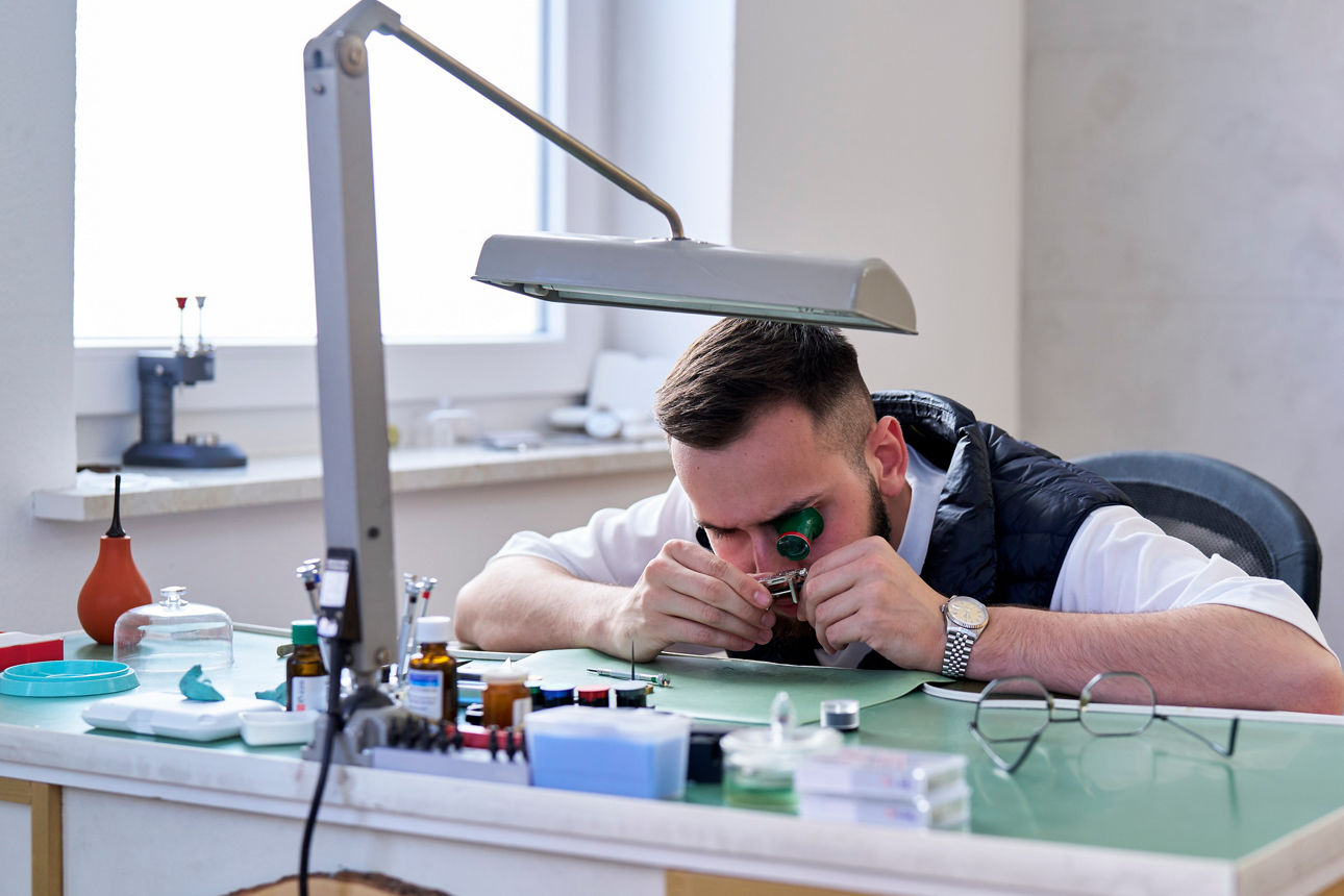 Max Müller sitzt an seinem Arbeitsplatz und arbeitet an einer Uhr