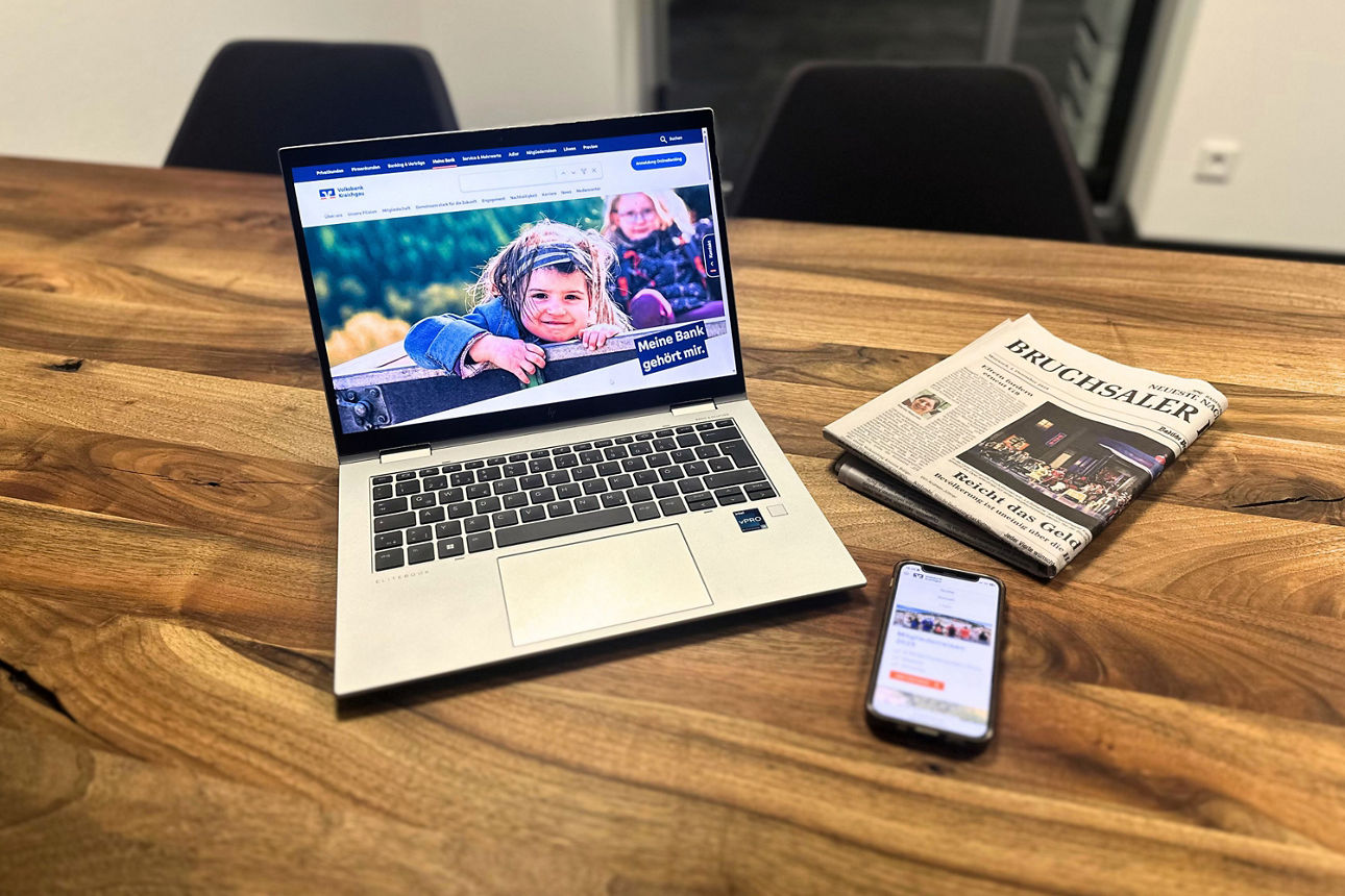 Ein Laptop, eine Zeitung und ein Handy liegen auf einem Tisch.