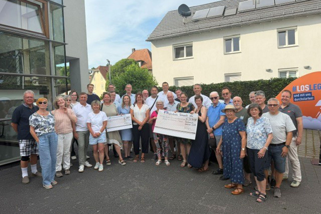Eine große Gruppe von Menschen, die im Freien posieren und einen symbolischen Scheck in den Händen halten