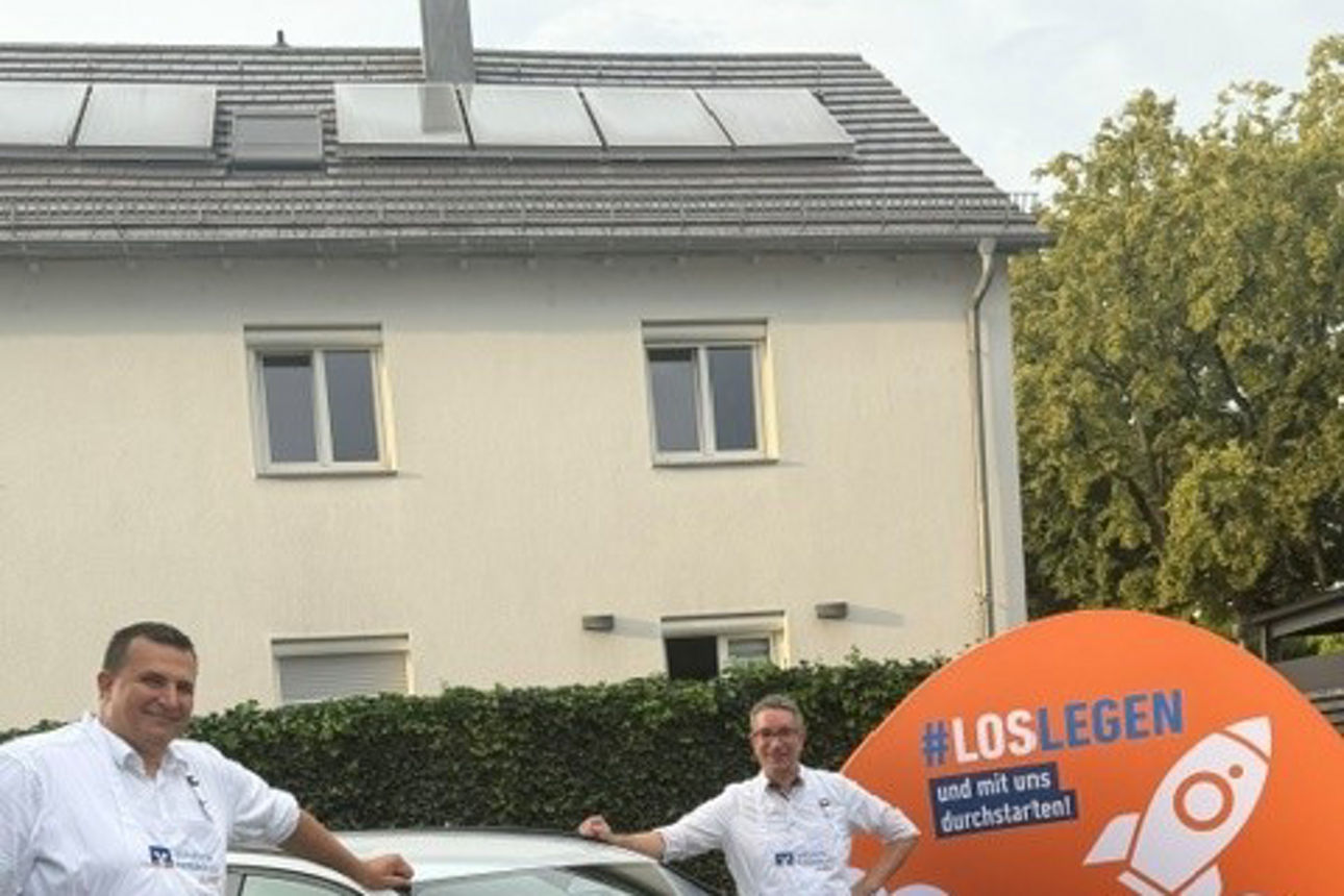 Zwei Männer in weißen Hemden stehen neben einem Audi-Fließheckmodell, das zu Werbezwecken ausgestellt ist.