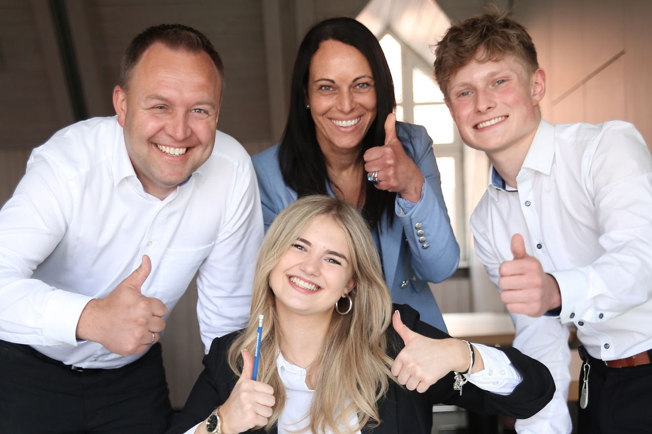 Vier Mitarbeiter und Mitarbeiterinnen lachen in die Kamera mit Daumen hoch Geste