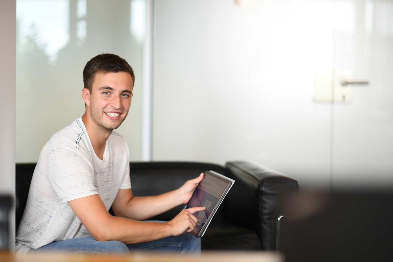 Ein Mann sitzt mit einem Tablet lächelnd vor einem unvollständig aufgebauten Bücherregal