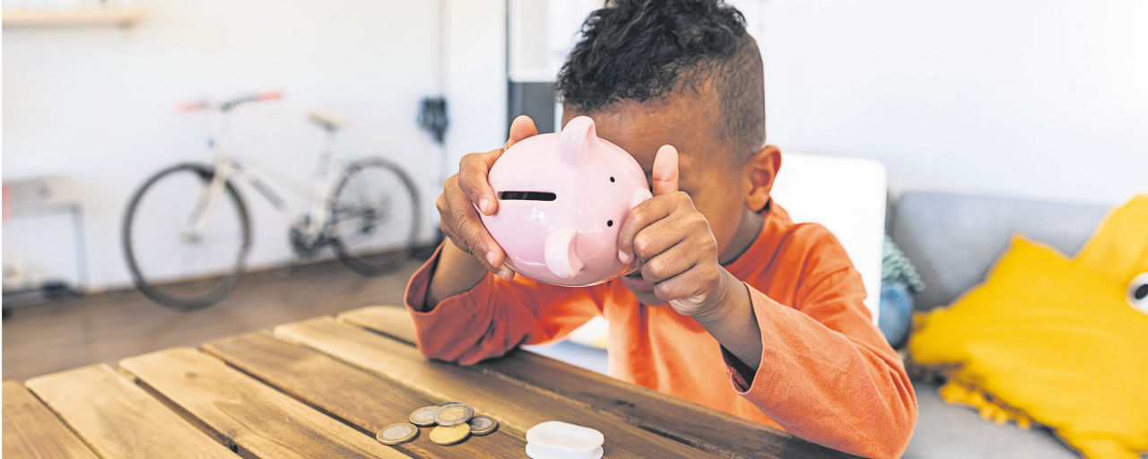 Kind sitz in einem Zimmer und versucht in ein Keramik-Sparschwein zu gucken