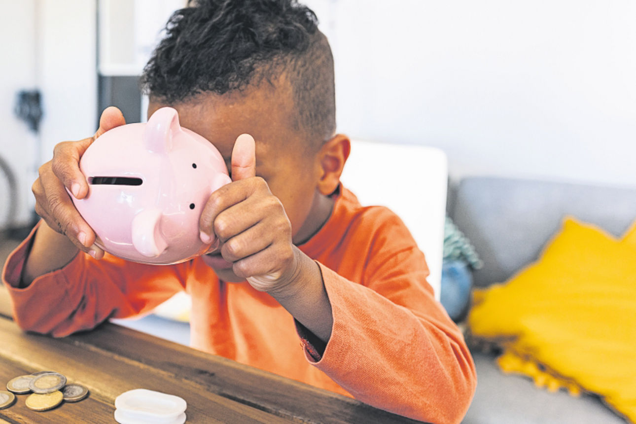 Kind sitz in einem Zimmer und versucht in ein Keramik-Sparschwein zu gucken