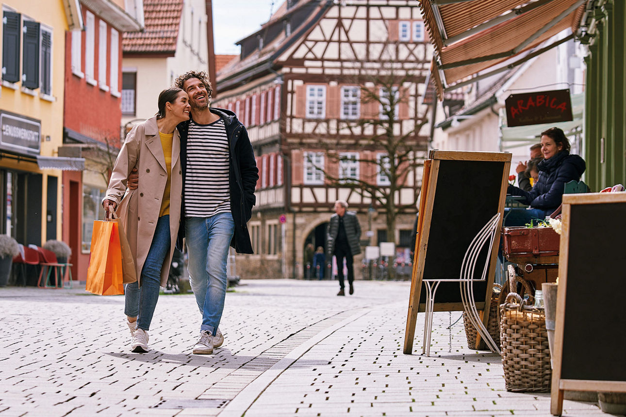 Ein glückliches Paar mit Einkaufstasche läuft durch eine gemütliche Fußgängerzone